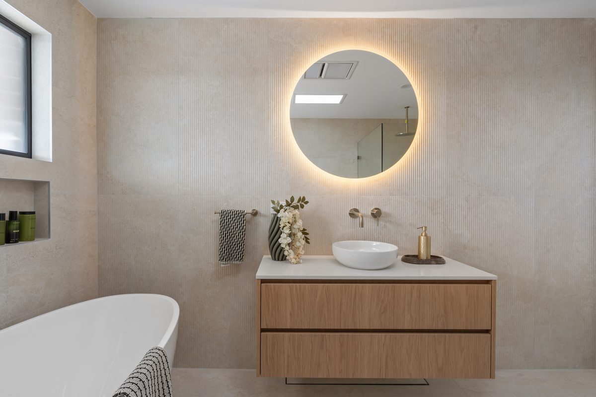 Bathroom renovation with backlit round mirror and freestanding b