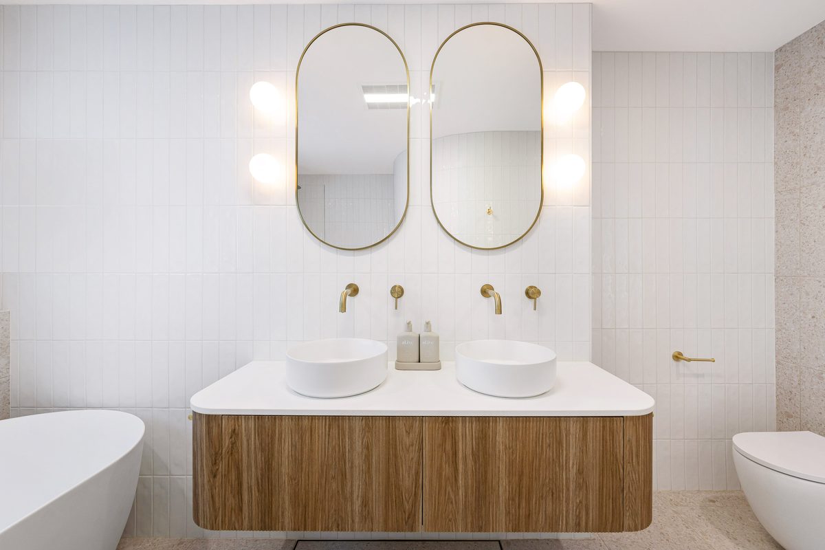 Bathroom renovation with gold-framed oval mirrors and freestandi